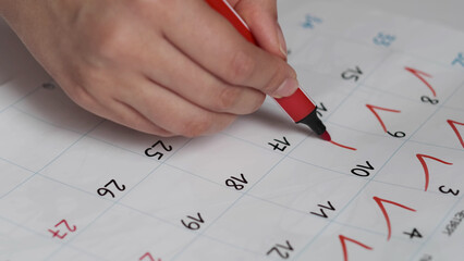 Blurred calendar page. Close-up female hand cross out days in calendar. Red circle marked with pen on a calendar sheet