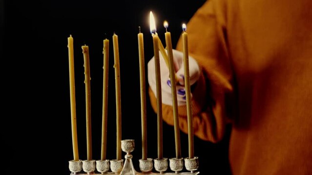 A woman's hand lights candles on the last day of Hanukkah from a shamash candle in a Hanukkah lamp