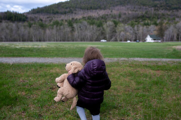 Toddler girl walks with her stuffy in only socks on a field