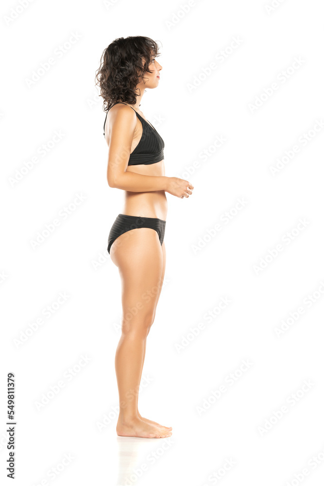 Canvas Prints Young exotic brunette woman in black bikini swimsuit posing on a white background. Profile, sidet view.