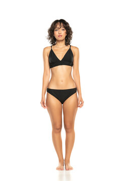 Young exotic brunette woman in black bikini swimsuit posing on a white background. Front view.