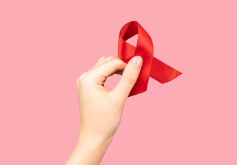 Red satin ribbon, bent loop in hand on pink background. HIV and AIDS awareness day, 1 December symbol
