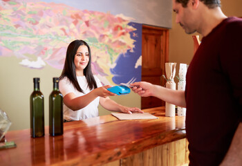 latin mid adult woman receiving electronic payment with customer's card in a small store