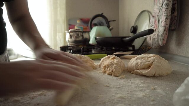 the cook gently and gently rolls out the dough on the floured kitchen table. dishes are standing in the background, close-up