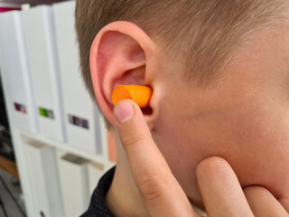 Boy inserting ear plugs into ears to get rid of noise in loud place