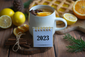 Calendar for 2023 and fragrant tea with orange and spices on a wooden table. Pie, lemons, oranges...