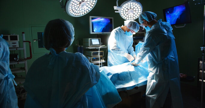 Multi-ethnic group of professional surgeons in uniform performing neurosurgery operation using medical instruments under lamps in operating room in hospital. Healthcare. Doctors and nurses concept