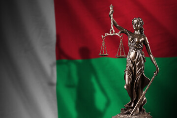 Madagascar flag with statue of lady justice and judicial scales in dark room. Concept of judgement...