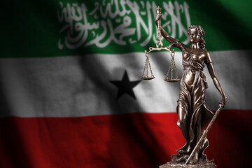 Somaliland flag with statue of lady justice and judicial scales in dark room. Concept of judgement...