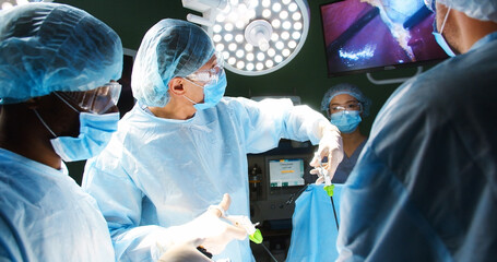 Close up of mixed-races professional doctors surgeons in uniform and mask performing operation...