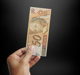 Male hand holding a 50 reais banknote in a studio black. Money from Brazil. 3d rendering.