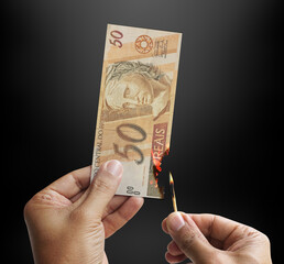 Burning money. Male hand setting a 50 reais bill on fire. Money from Brazil. 3d rendering.