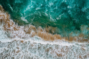 Wild high waves of Atlantic Ocean,turquise water,sandy beach in Portugal.Summer vacation travel concept.Top down view.Aerial view of wave breaking the shore.Empty paradise beach.Natural background