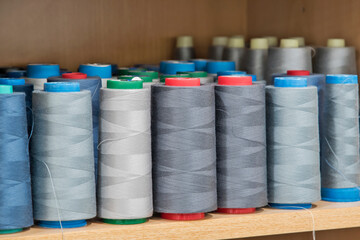 Sewing thread cones of different shade of colors on shelf in sewing studio closeup