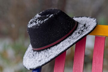The black hat on a colorful chair, covered with snow, during a winter storm