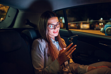 Business woman using smartphone while sitting in a backseat of a car at night