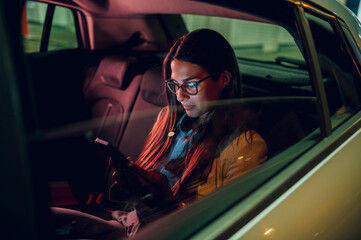 Business woman using smartphone while sitting in a backseat of a car at night