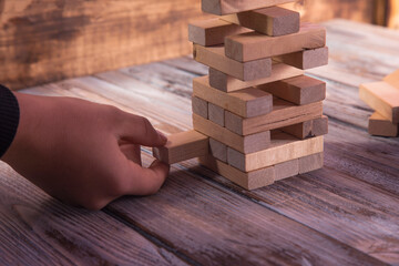 Close-up hand takes one block on a wooden block tower.