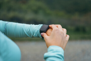 A fitness girl is looking at her smart watch to see how many steps she has been taking, as well as...
