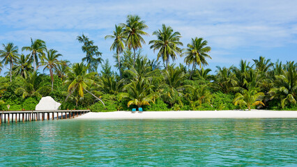 view on resort island from distance, beautiful tropical beach line with many palm trees and blue...