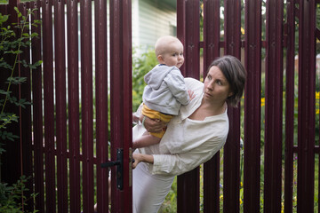Curious woman with a baby peeps openint the gate of fence