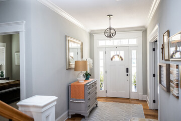 An open large and wide interior front door hallway foyer with transom, hanging light fixture, coastal colors and entry way table and wood floors - obrazy, fototapety, plakaty
