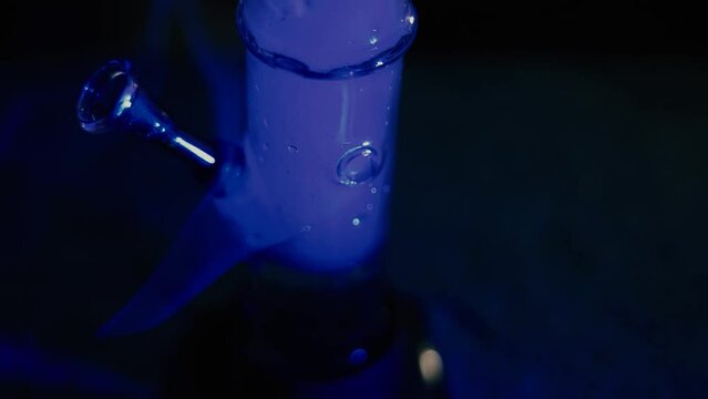 Male hands clog a bong with marijuana. Drugs and drug addict. The man smokes weed. Neon blue light. CBD or THC.