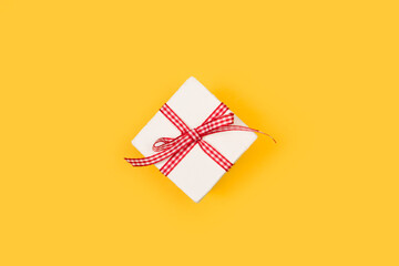 Caja de regalo blanca con un lazo de color rojo y blanco sobre un fondo amarillo liso y aislado. Vista superior y de cerca. Copy space