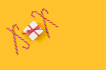 Caja de regalo blanca con un lazo de color rojo y blanco junto a bastones de caramelo sobre un fondo amarillo liso y aislado. Vista superior y de cerca. Copy space