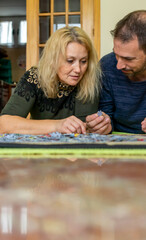 Fototapeta premium Couple in their 40s spending time together away from technology doing a puzzle lying on the floor, reconciliation, couples therapy.