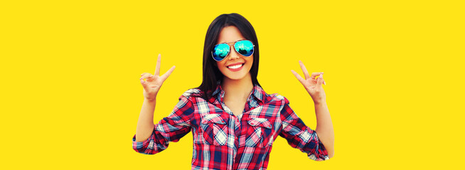 Portrait of beautiful happy smiling young brunette woman in sunglasses on yellow background