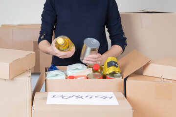 Volunteer woman collecting food into donations box. Cardbox full of grocery products. Donation,...