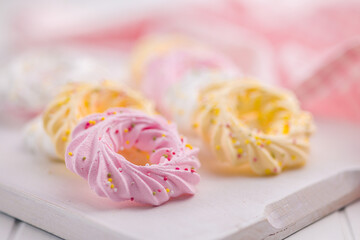 Different colors meringues with sprinkles on white table.