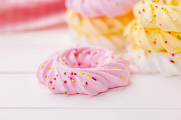 Different colors meringues with sprinkles on white table.