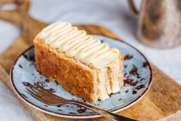 French dessert called Mille Feuille or Napoleon cake on rustic wooden board. Layered tasty cake with vanilla cream and puff pastry.