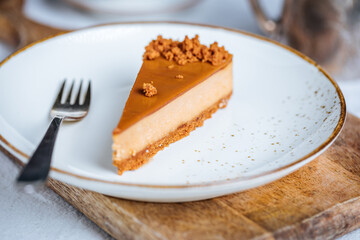 A piece of caramel cheesecake with cookie crumbs on top. Creamy three layer cake on bright plate. Popular American dessert.