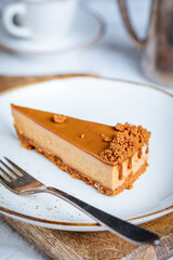 A piece of caramel cheesecake with cookie crumbs on top. Creamy three layer cake on bright plate. Popular American dessert.