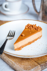 A piece of caramel cheesecake with cookie crumbs on top. Creamy three layer cake on bright plate. Popular American dessert.
