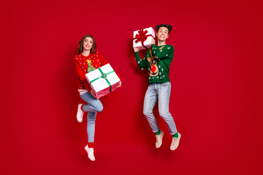 Full length portrait of two excited crazy people arms hold festive package giftbox jumping isolated on red color background