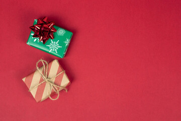 Two christmas and new year presents or gifts on red background with copy space, top view. Gift boxes wrapped in green and craft red paper with bows. Postcard and banner.