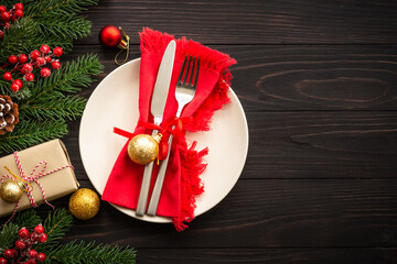 Christmas table setting with craft plate, cutlery, gift box and christmas decorations on dark...