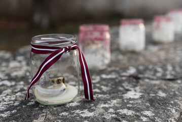 Candles in jars and ribbon in red and white Latvian flag color. - obrazy, fototapety, plakaty