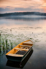 a foggy pond and a lonely boat in the foreground, an idyll of autumn