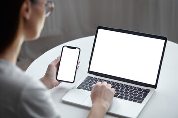 Mockup white screen laptop and mobile phone woman using computer while sitting at table at home, back view