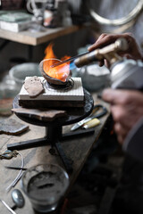 A craftsman jeweler is manipulating some melted jewels with clamps and a blowtorch