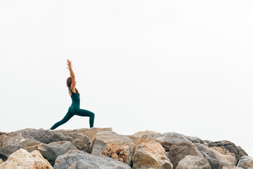 Portrait of fit woman practicing various yoga asanas  outdoors by the sea, doing crescent pose or high lunge, ashta chandrasana in nature. Energy, flexibility, strength and power concept. Copy space
