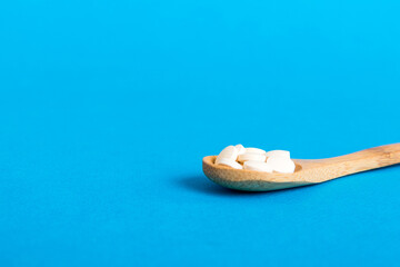 Heap of white pills on colored background. Tablets scattered on a table. Pile of red soft gelatin capsule. Vitamins and dietary supplements concept