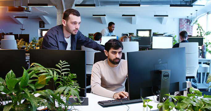 Multiethnic males coworkers talking and discussing IT project at computer screen. Coworking space office. Men developers chatting and having discussion. Startuppers communication. Startup.