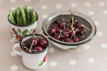 Washed sweet cherry in a metal enamel mug, green young peas