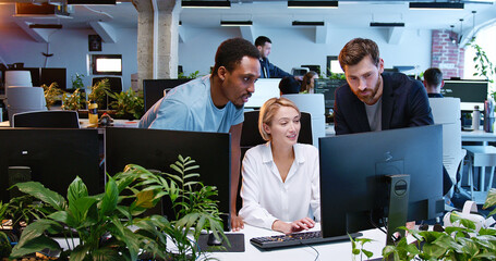 Woman with coworkers discussing working project at computer in coworking space. Multiethic team of...